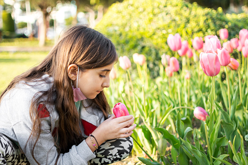 Cute girl smelling to tulip flower with protective mask to park