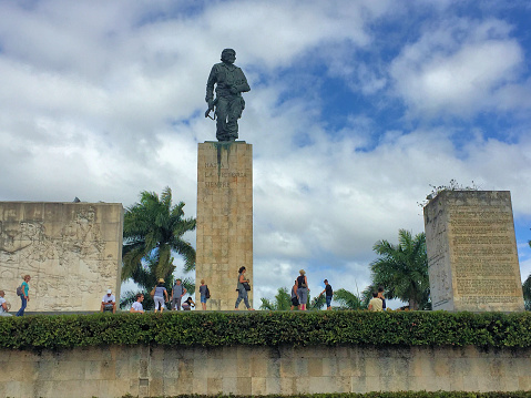 People are walking in front of the statue of Che Guevara surrounded with some palm trees on a sunny day with cumulus clouds in the city of Santa Clara in Cuba December 21,2016