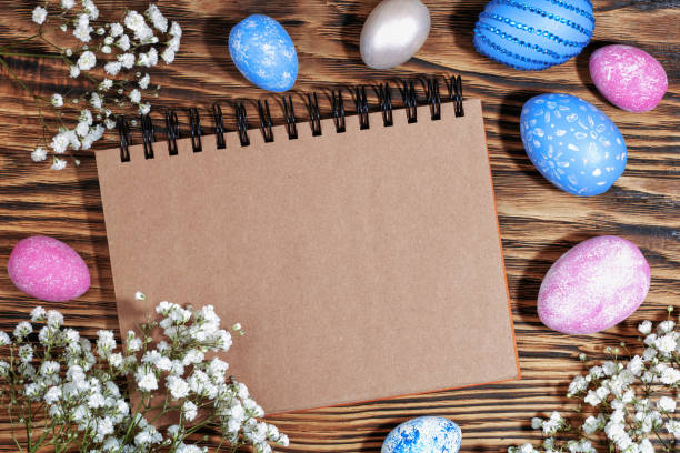 istock Craft notebook for text on trendy wooden eco background with pink and blue Easter eggs and white flowers. Top View. Copy space 1310415658