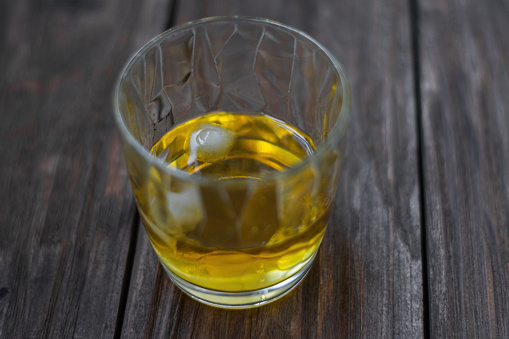 Close-up photo of a glass of whiskey with ice on an old wooden table