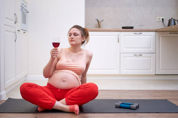 femme enceinte faisant la forme physique à la maison et regardant le vin rouge dans un verre - eastern european caucasian one person alcoholism photos et images de collection