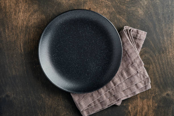 istock Empty black plate, cutlery and napkin on old wooden table top view. Table setting. 1310420875