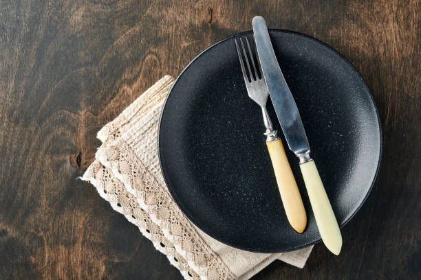 istock Empty black plate, cutlery and napkin on old wooden table top view. Table setting. 1310421418