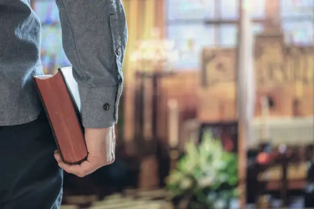 Man holding holy bible in church with alter in background concept for religion, praying, education and bible study