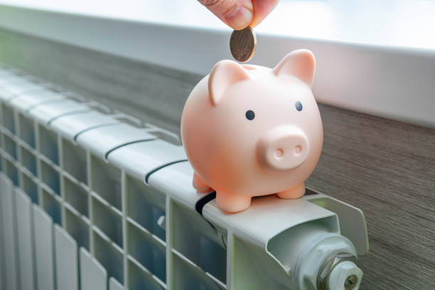 concept of paying for heating in homes with a cold climate. Cash money is lying on a white metal radiator near the window. The concept of paying for heating in homes with a cold climate. piggy bank pig on a white metal radiator. The concept of saving on utilities budget cut stock pictures, royalty-free photos & images