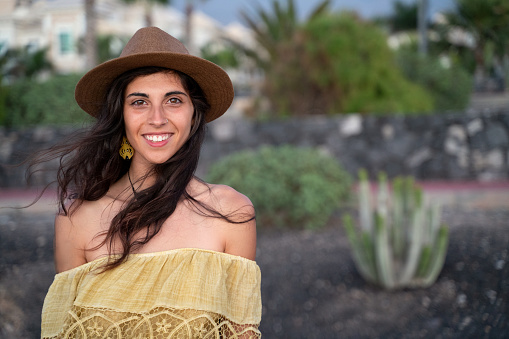 Happy latin woman with beautiful smile wearing fashionable hat and looking at camera. Young brunette woman enjoying vacation during summer. Cheerful girl. Real people emotions.