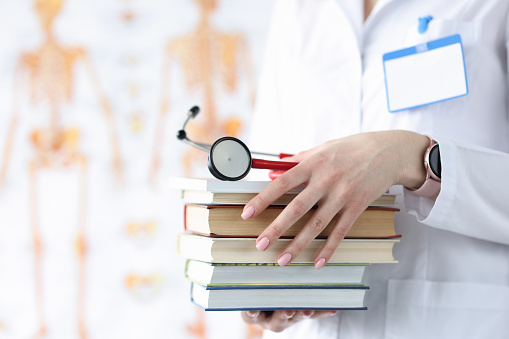 Doctor hands are holding stack of books and stethoscope. Medical education concept