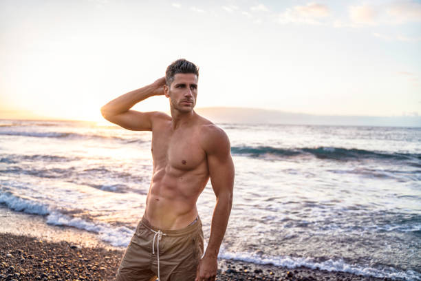 handsome young muscular italian man posing shirtless on the beach, sunset summer time. - shirtless imagens e fotografias de stock