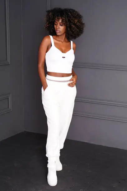 Young beautiful and fashionable african woman with afro hair, wearing sporty comfy clothes, posing over dark studio background.