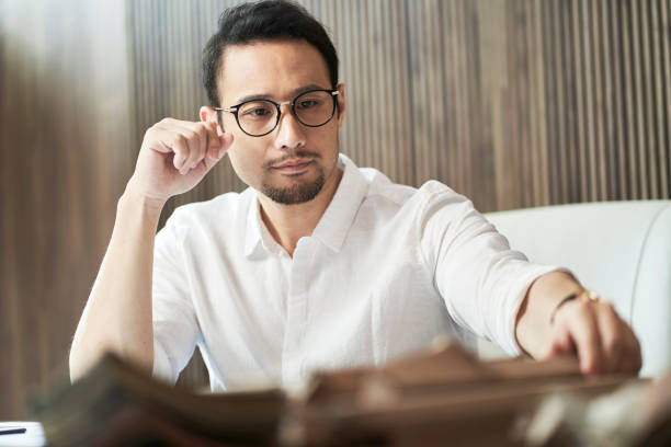 Asian bearded designer sitting, thinking and sketching ideas indoors stock photo
