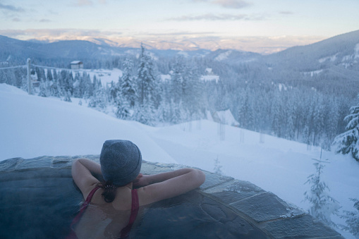 Young Caucasian woman resting in hot tub with view on mountains in winter
