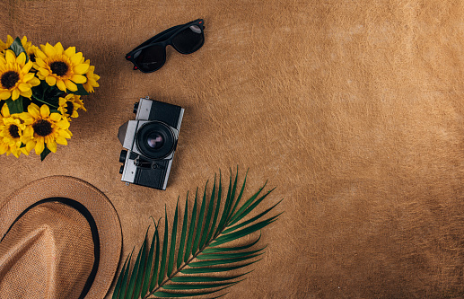 Camera, hat and sunglasses on brown background. Flat lay concept.