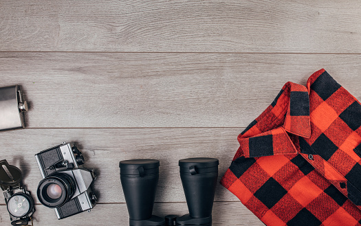 Binocular, compass, camera, plaid shirt and flask on wooden background.