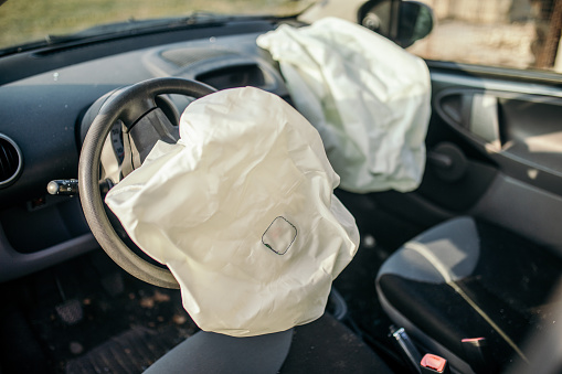 Car crashed in an accident on a highway or city street. Broken glass is all around and the airbag is open. Pieces of a car equipment like radio, buttons and control table fell off because of the strength of the crash.