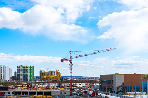 Construction of a new multi-storey building in the city, red construction crane on a blue cloudy sky background, construction site, New High-Rise Buildings