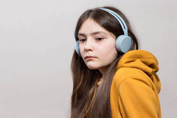 a sad teenage girl, 12-13 years old, sits in headphones sweatshirt on a white background copy space for text. - 12 13 years fotos imagens e fotografias de stock