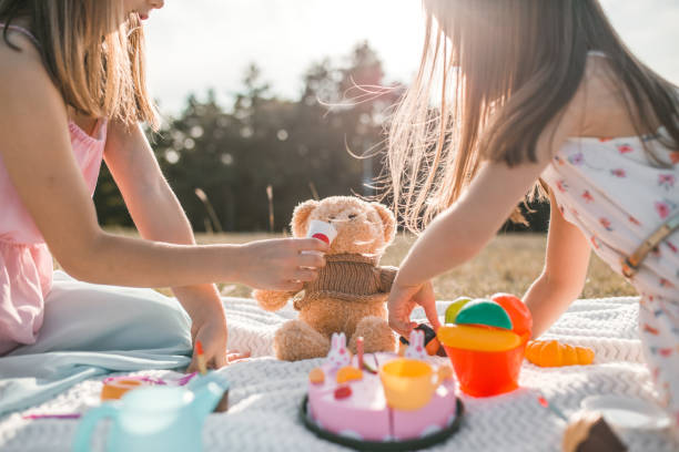 istock Two sisters feeding their teddy bear on a picnic in park 1310436434