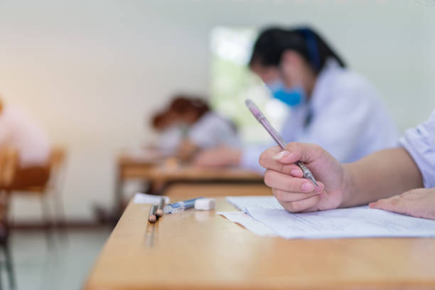 studenti asiatici che testano l'esercizio d'esame al liceo o all'università in sala prove. le mani tengono la carta del documento di lettura della matita su scrivanie di legno in classe, torna a scuola per la misurazione della valutazione - scholastic aptitude test foto e immagini stock