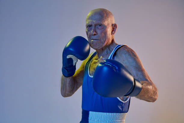 homme aîné utilisant la boxe de sportswear d’isolement sur le fond de studio de gradient dans la lumière de néon. concept de sport, d’activité, de mouvement, de bien-être. copyspace, annonce. - boxing glove sports glove isolated old photos et images de collection