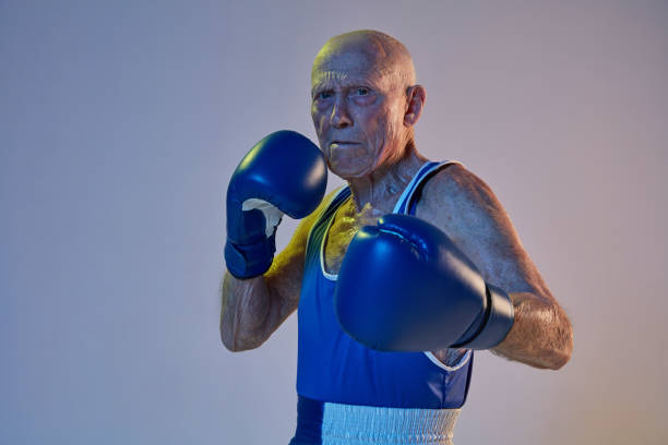 Aggressive old man in sportswear training with boxing bag in gym