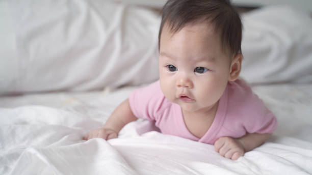 bébé asiatique heureux apprenant à ramper sur le lit doux blanc. expression faciale de bébé de 3 mois. beau et sourire bébé.. - baby yawning asian ethnicity newborn photos et images de collection