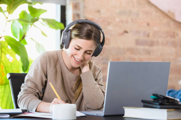 istock Young adult woman enjoys music while working on schoolwork 1310450559