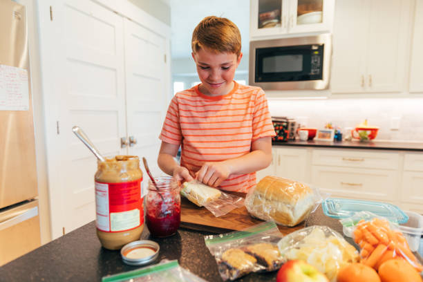 Preparing School Lunch A boy prepares a school lunch consisting of peanut butter and jelly sandwich, chips, cookies, fruit, carrots and putting them in plastic bags. making a sandwich stock pictures, royalty-free photos & images