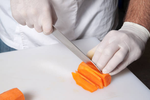 the chef in gloves cuts carrots on a plastic board