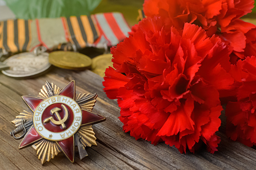 Victory Day.Order of the red star with the Russian inscription Patriotic war on a wooden background with red carnations.Celebration on may 9.Memorial day.Greeting card.copy space