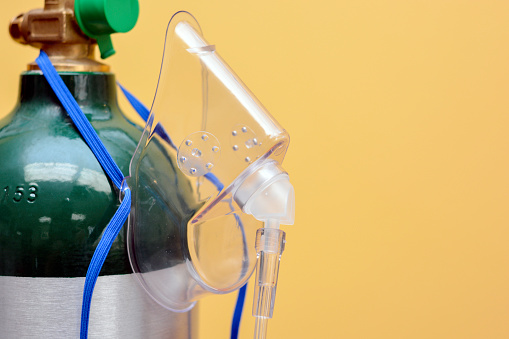 Close-up at angle of medical oxygen mask hanging from oxygen tank valve on yellow background