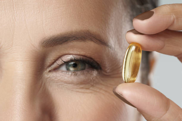 mujer de mediana edad sosteniendo cápsula con una fuente de pescado o aceite de krill de ácidos grasos omega-3 - fish oil fotografías e imágenes de stock