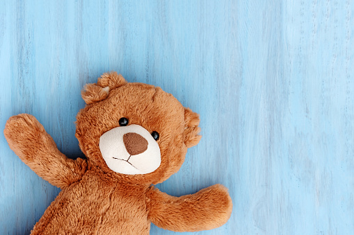 Cute stuffed toy teddy bear lies on blue wooden textured background with copy space, horizontal photo, top view.