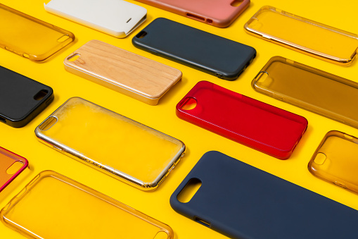 Pile of multicolored plastic back covers for mobile phone. Choice of smart phone protector accessories on yellow background. A lot of silicone phone backs or skins next to each other