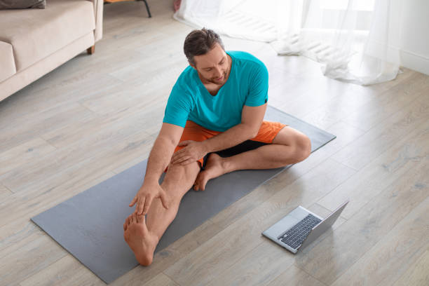 istock Man in front of a laptop is doing stretching at home. He uses an online tutorial. Online yoga and Pilates classes during quarantine 1310476810