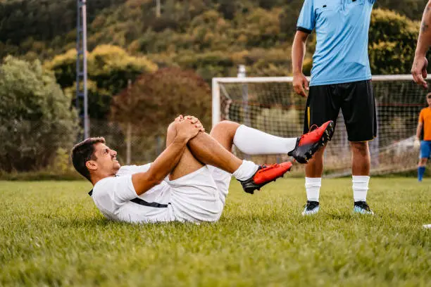Soccer player lying on field and holding his injured painful knee.
