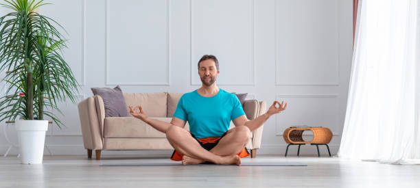 istock Photo of a middle-aged man meditating in home interior. Format 20:9 1310476904