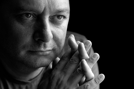 Black and White portrait of 40-45 years old serious thoughtful mature man without beard. The main light source is daylight. The photo was shoot indoors with a full frame mirrorless digital camera.The model hand is seen in frame.His hand is on his head.