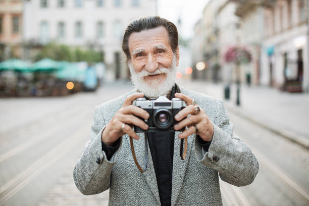 istock Senior man holding old photo camera while standing outdoors 1310485279