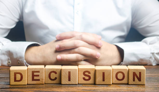 istock Man folded his hands on a background of blocks with the word Decision. Make the right decision, the answer to the question. Reasoning, weighing results and consequences. Authoritative opinion. 1310486680