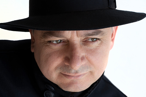 Portrait of stylish mature man with his classic round hat. He has no beard. He is completely in black.