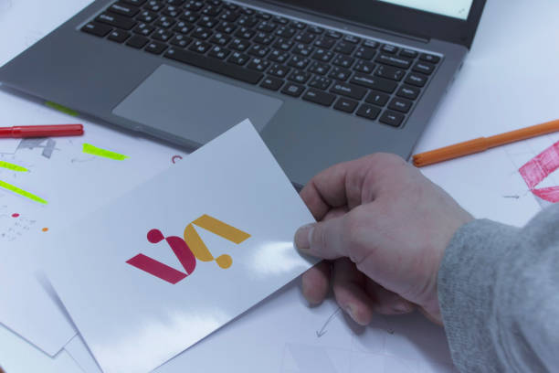 istock Creative workplace of a Graphic Designer. A man in the office is developing a logo on the table against the background of printed sketches and a laptop. 1310490194