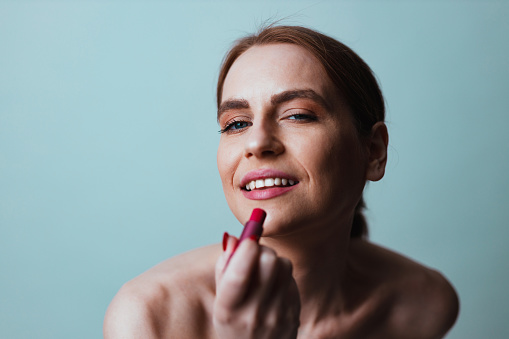 Portrait of a beautiful young woman applying pink color lipstick against a white background