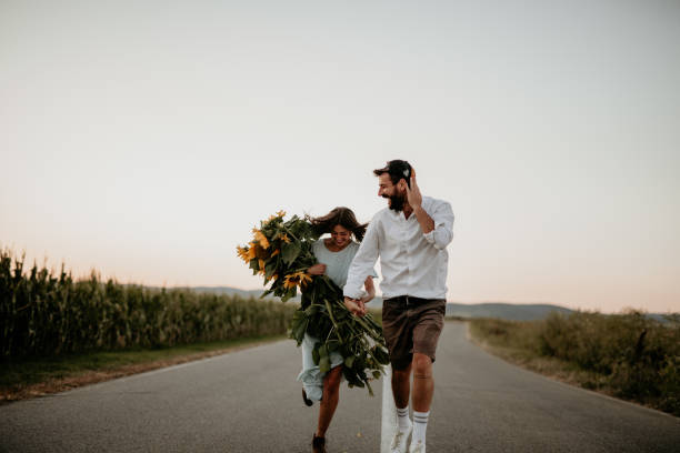 Loving couple retro wedding dressed running on the countryside road in the middle of the fields.