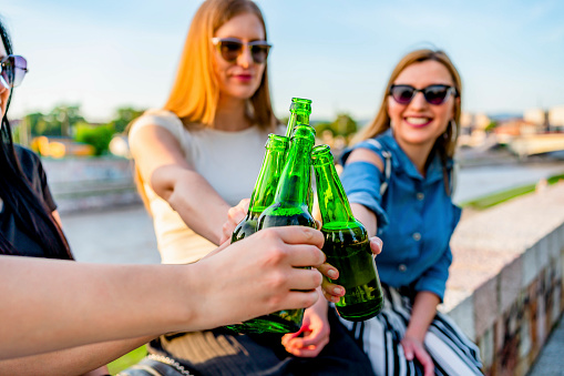 Young smiling female friends toasting with beer bottles