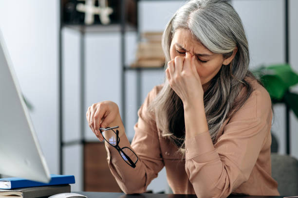 istock Overworked tired older lady holding glasses feeling headache, after computer work. Sad mature gray haired fatigue woman is massaged eyes at workplace 1310497192