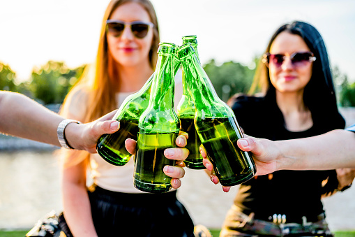 Young cheerful female friends toasting with beer bottles