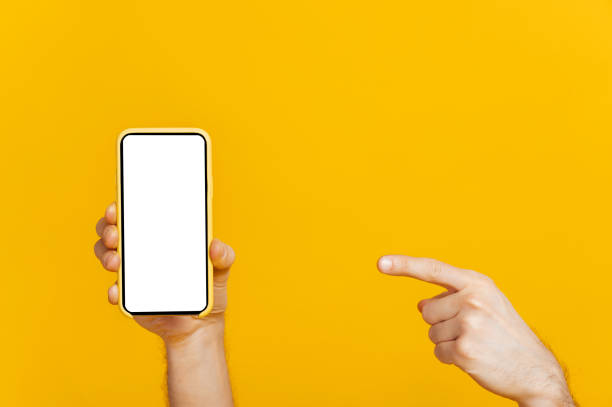 istock Touchscreen smartphone, cellphone with blank white screen for presentation in male hand, finger points to mobile phone, on isolated orange background, copy space, mockup concept 1310500801