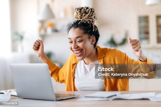 Overjoyed Excited African American Girl With Dreadlocks Freelancer Manager Working Remotely At Home Using Laptop Looks At Screen With Surprise Smiling Face Gesturing With Hands Got A Dream Job Stock Photo - Download Image Now