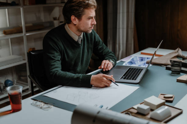 istock Handsome Caucasian Male Architect Drawing on a Project Plan in his Office while Looking at Something on his Laptop Computer 1310504724
