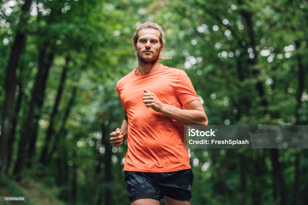 Young Caucasian Sportsman Running in the Forest A young sportsman running in the forest, training for a marathon Men Stock Photo